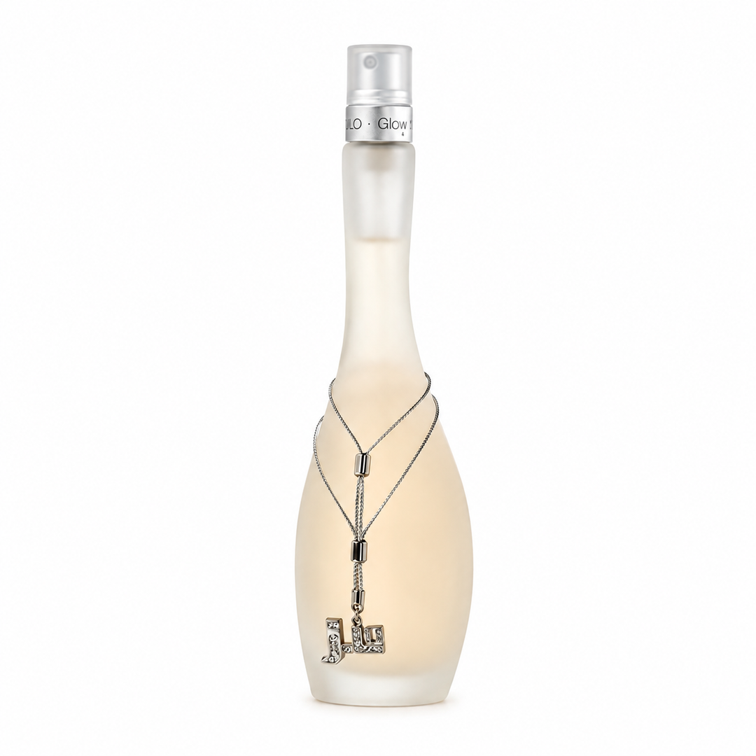 A frosted glass perfume bottle with a pale peach tint, featuring a silver spray nozzle and wrapped with a silver chain necklace displaying a rhinestone-embellished 'J' pendant, on a solid white background.